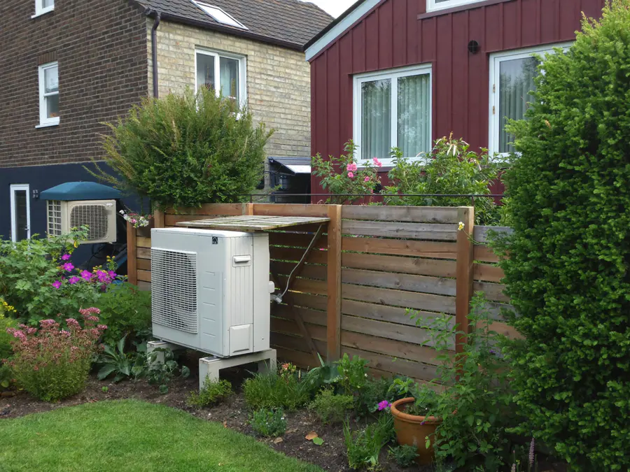 Buitenunit naast een houten schutting in een tuin tussen twee woningen