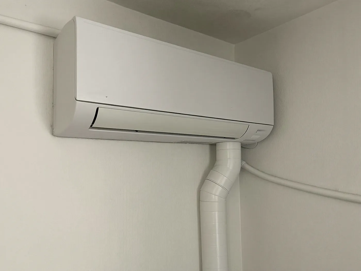 Binnenunit met de afvoer van het condenswater in een witte goot langs de muur