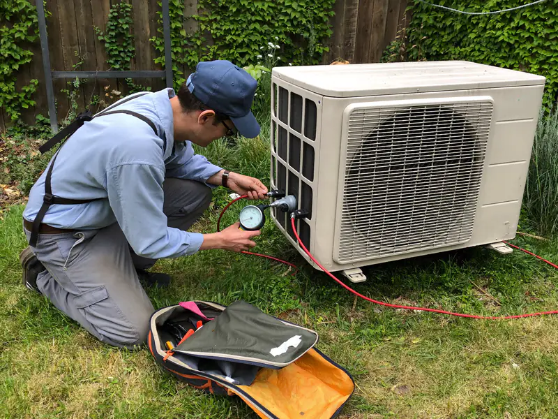 Monteur met een manometer aan de aansluitingen van een buitenunit in een tuin