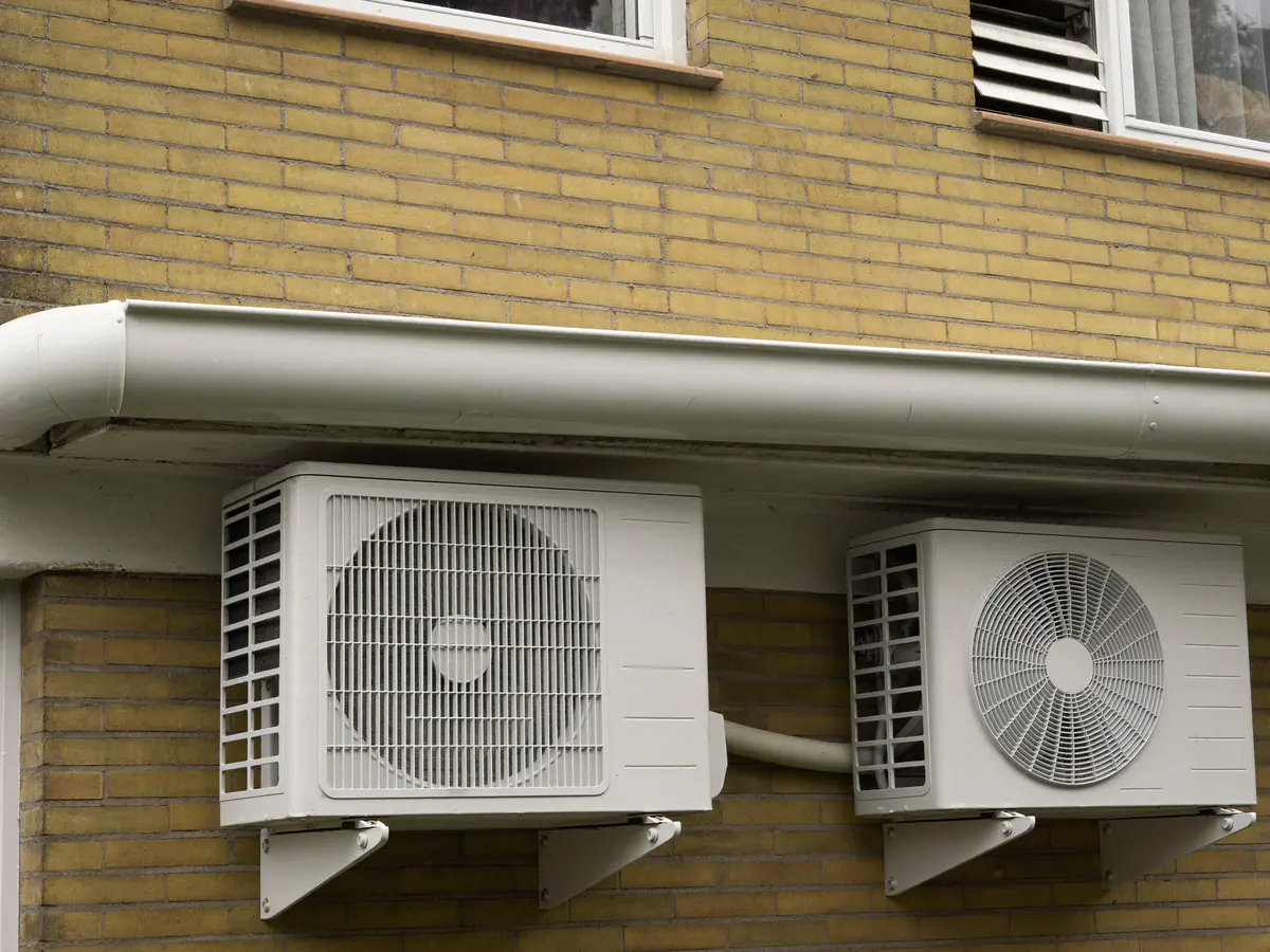 Twee buitenunits op beugels aan een gele bakstenen gevel onder een brede goot