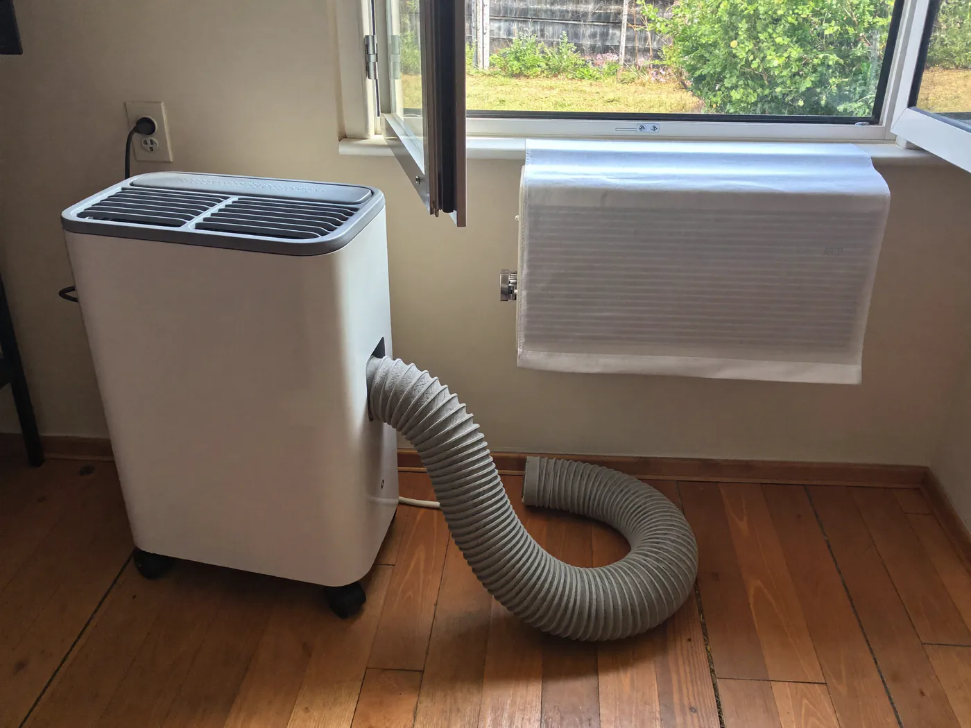 Mobiele airco op wieltjes in een slaapkamer met een slang naar het raam