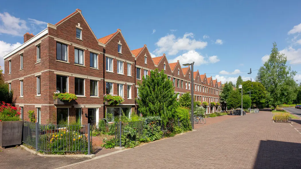 Rij bakstenen woningen met puntgevels langs een brede stoep met bomen