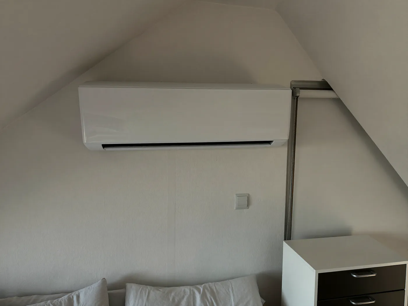Slaapkamer onder een schuin dak met een binnenunit aan de rechte wand