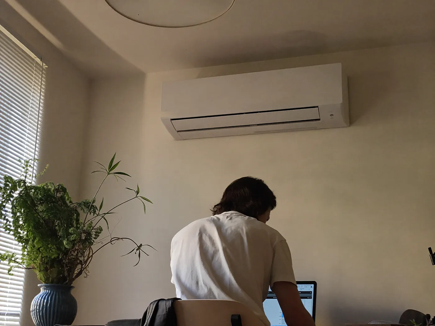 Man aan een bureau met laptop in een kamer met een airco aan de wand